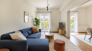 A modern living room with a sofa, ottoman, coffee table, and a TV stand. - Green Oasis 2BR Apartment in Pangrati (Athina)