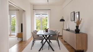 A dining area with a table, chairs, a cabinet, and a window with curtains. - Green Oasis 2BR Apartment in Pangrati (Athina)