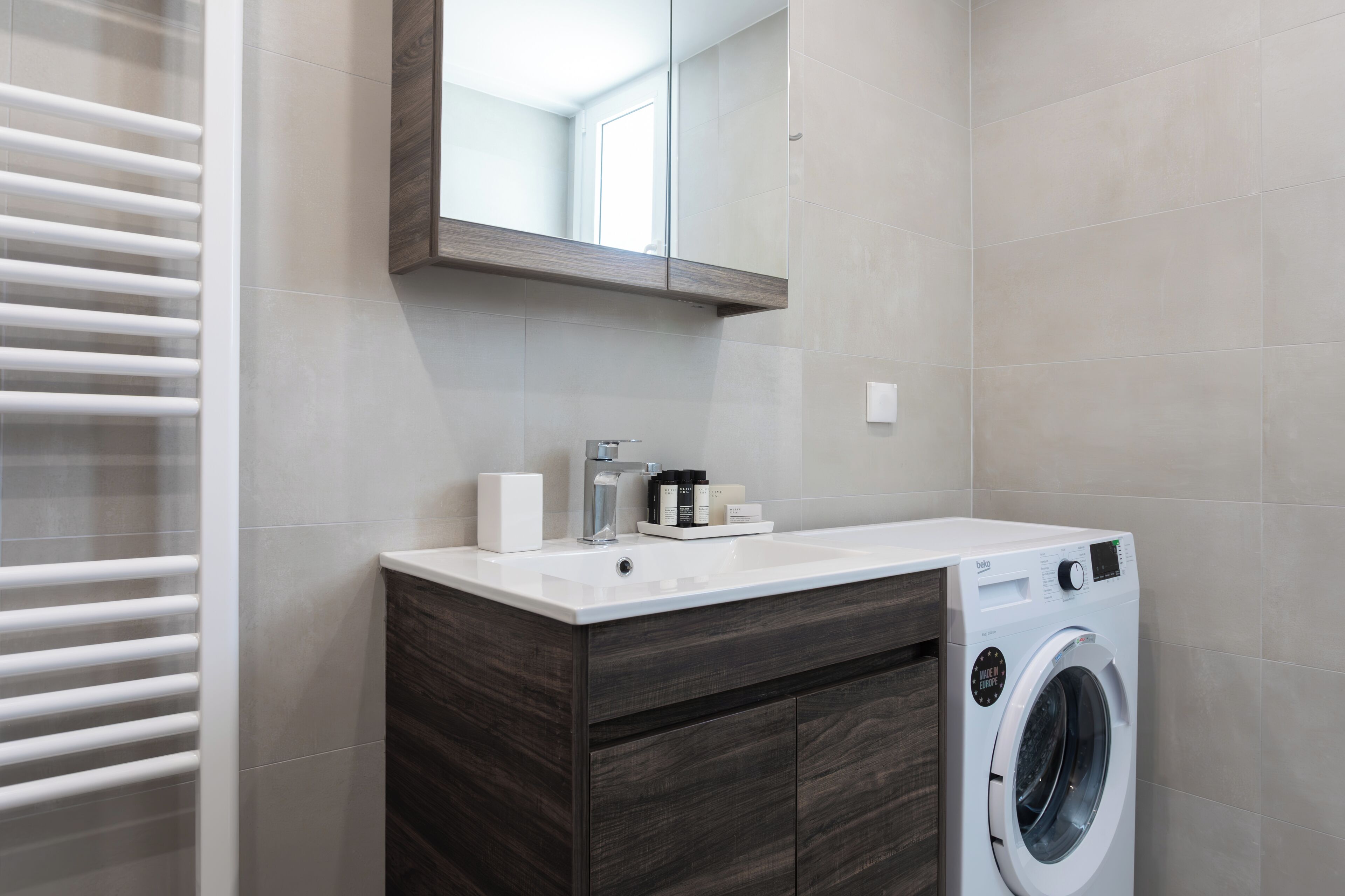 A modern bathroom with a built-in washing machine, a mirror, and a towel rack.