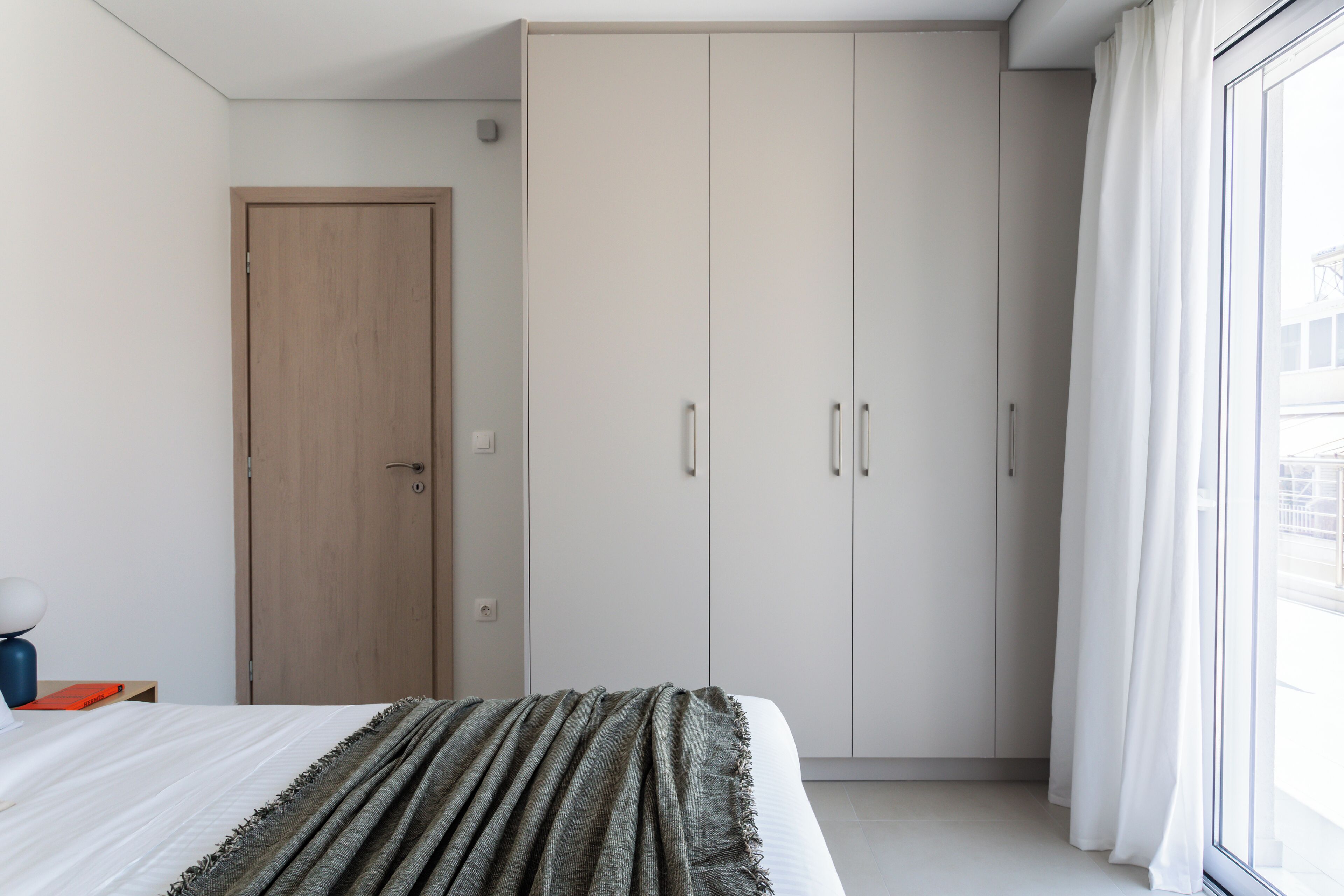 A bedroom with a bed, a wardrobe, a door, and a window with curtains.