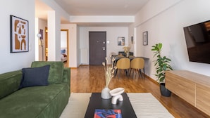 Una sala de estar moderna con un sofá verde, una mesa de centro con una revista, un comedor con sillas y un televisor en la pared.