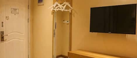 A hotel room with a wooden vanity, a mirror, a television mounted on the wall, and a door with a sign.