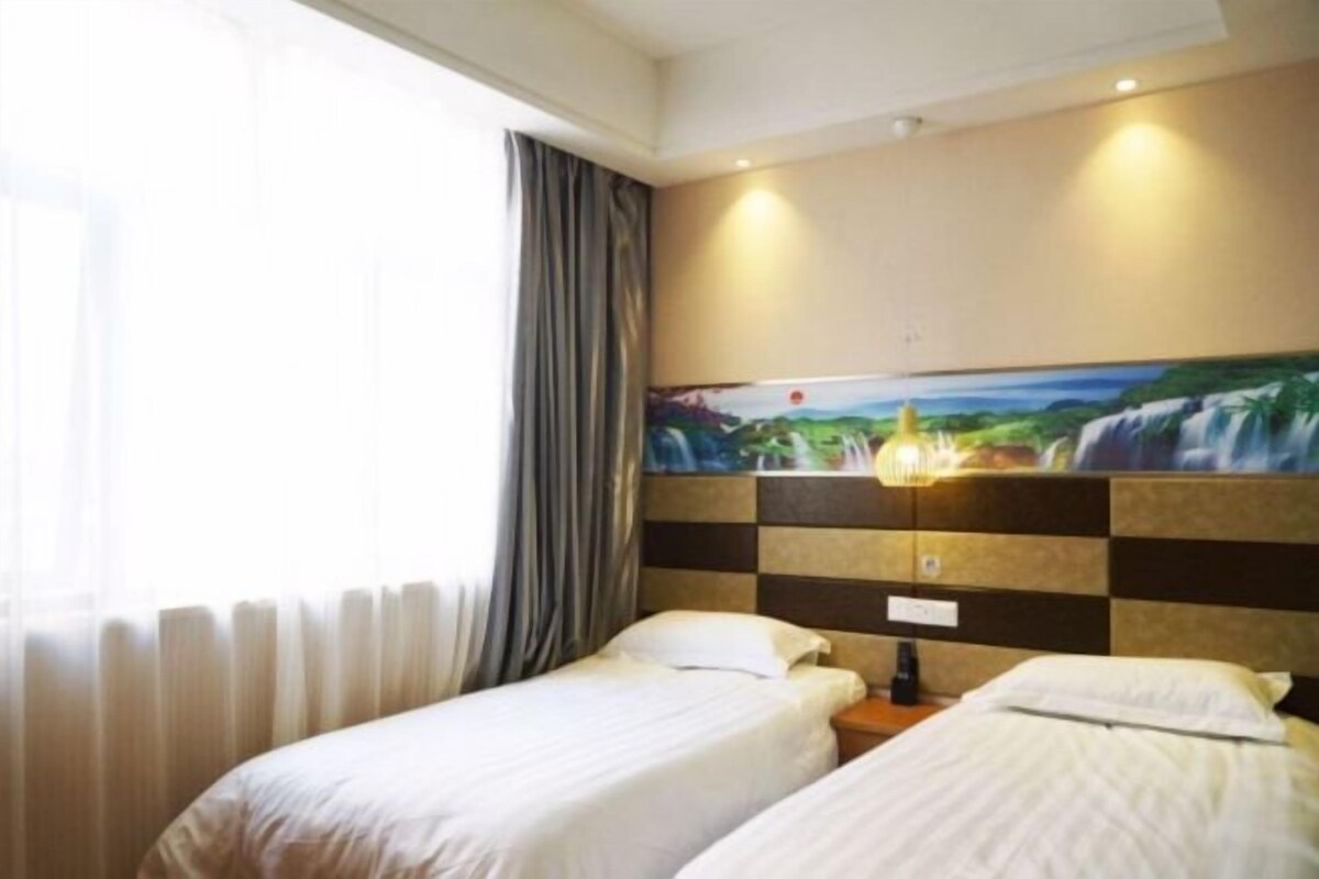 Habitación de hotel con dos camas individuales, un cuadro en la pared, una ventana con cortinas y un radiador.
