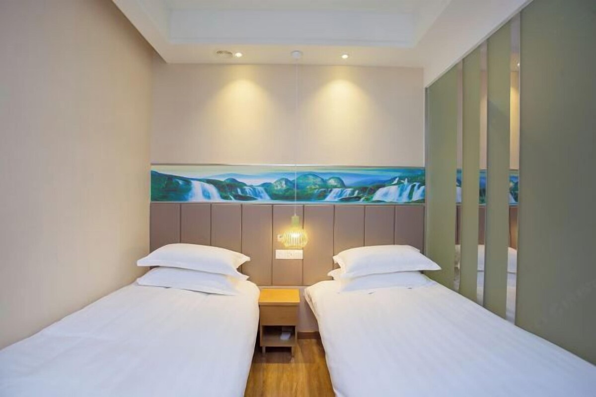 Habitación de hotel con dos camas individuales, un cuadro de una cascada en la pared y una mesita de noche pequeña con una lámpara.