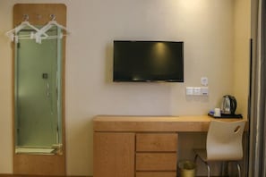 Quarto com escrivaninha de madeira, televisão na parede, espelho e cadeira.