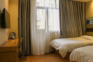 A hotel room with two beds, a desk, a chair, and a television.