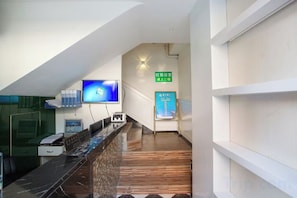 A hotel reception area with a reception desk, a flat-screen TV, and a staircase leading to an upper floor.