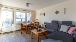 Una sala de estar con un sofá gris, una mesa de centro de madera y un comedor con una mesa y sillas.