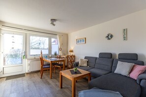 A living room with a grey sofa, wooden coffee table, and a dining area with a table and chairs.