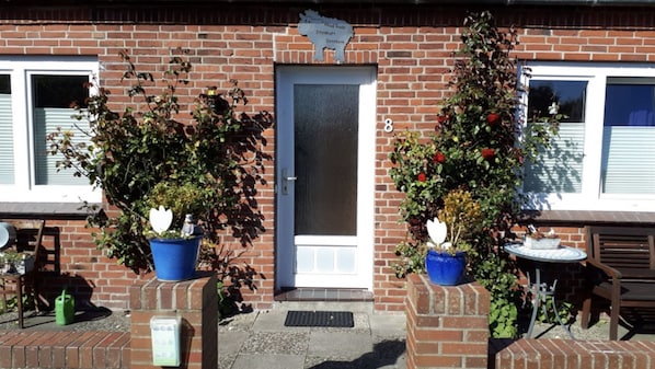 A brick building with a door, two potted plants, a small table, and a bench.
