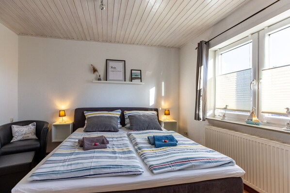 Un dormitorio con dos camas, lámparas de noche, una mesita de noche, una silla y una ventana con persianas.