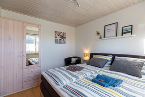 A bedroom with a bed, a wardrobe, a nightstand, a lamp, and wall art.