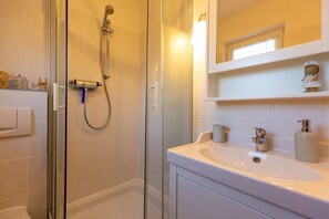 A modern bathroom with a glass shower enclosure, a white sink with a gold faucet, and a mirror above the sink.