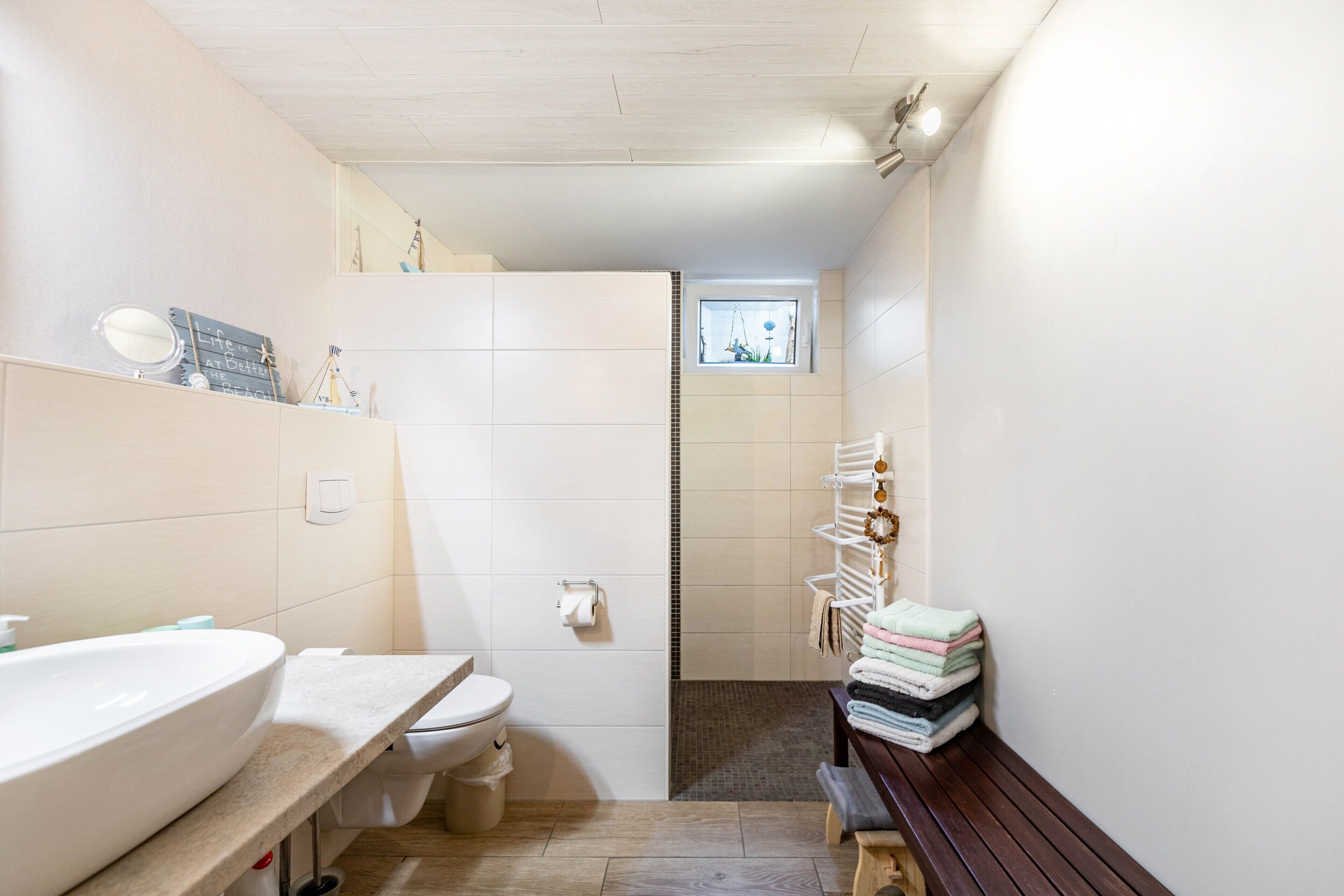A bathroom with a sink, toilet, and a bench with towels.