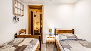 A room with two wooden beds, a wooden headboard, a small table with a lamp, and a wall-mounted shelf with a life preserver.