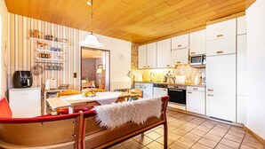 A kitchen with white cabinets, a dining table with chairs, a bench with a fur throw, and a hanging light fixture.