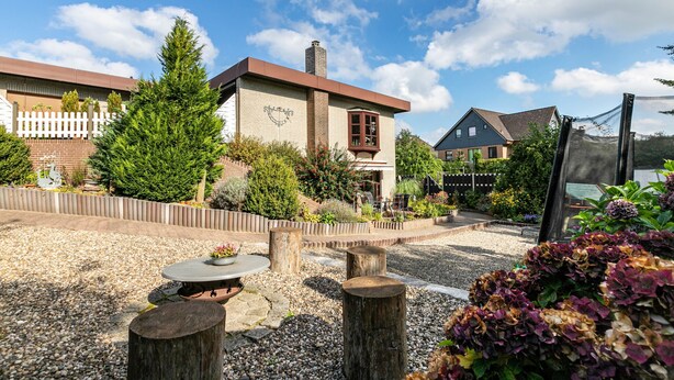 A building with a brick facade, a white picket fence, and a garden with gravel paths and wooden posts.