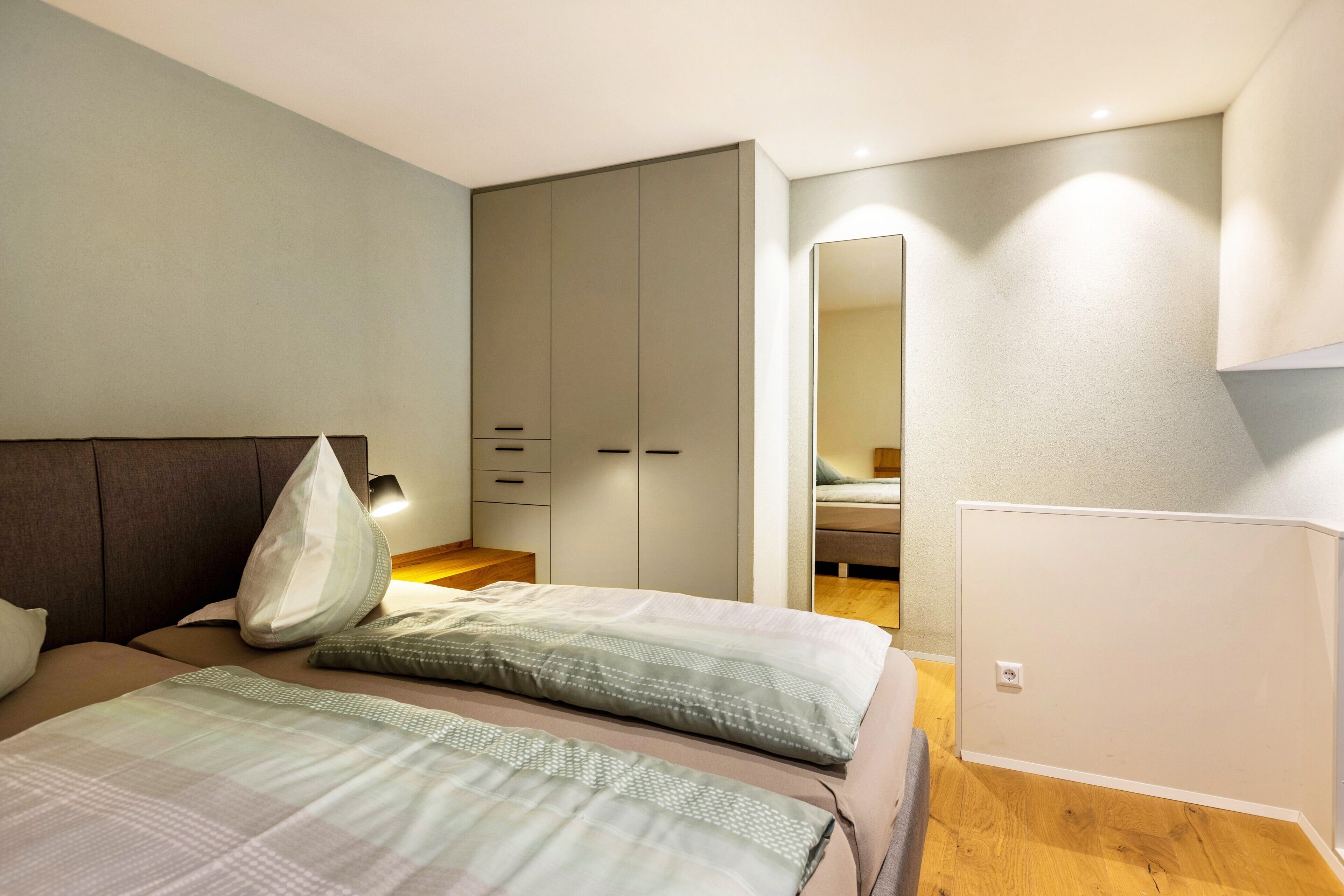 A bedroom with a bed, a wardrobe, a mirror, and a bedside table.