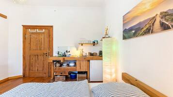 Ein kleines Zimmer mit Holztür, einer Küchenzeile, einem Bett mit gestreifter Bettwäsche und einem Landschaftsbild.