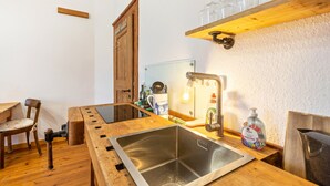 Een keuken met een houten tafel, een roestvrijstalen spoelbak, een houten stoel en een plank met glazen.