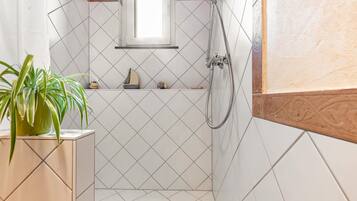 A bathroom with white tiled walls, a shower, a small window, and a potted plant.