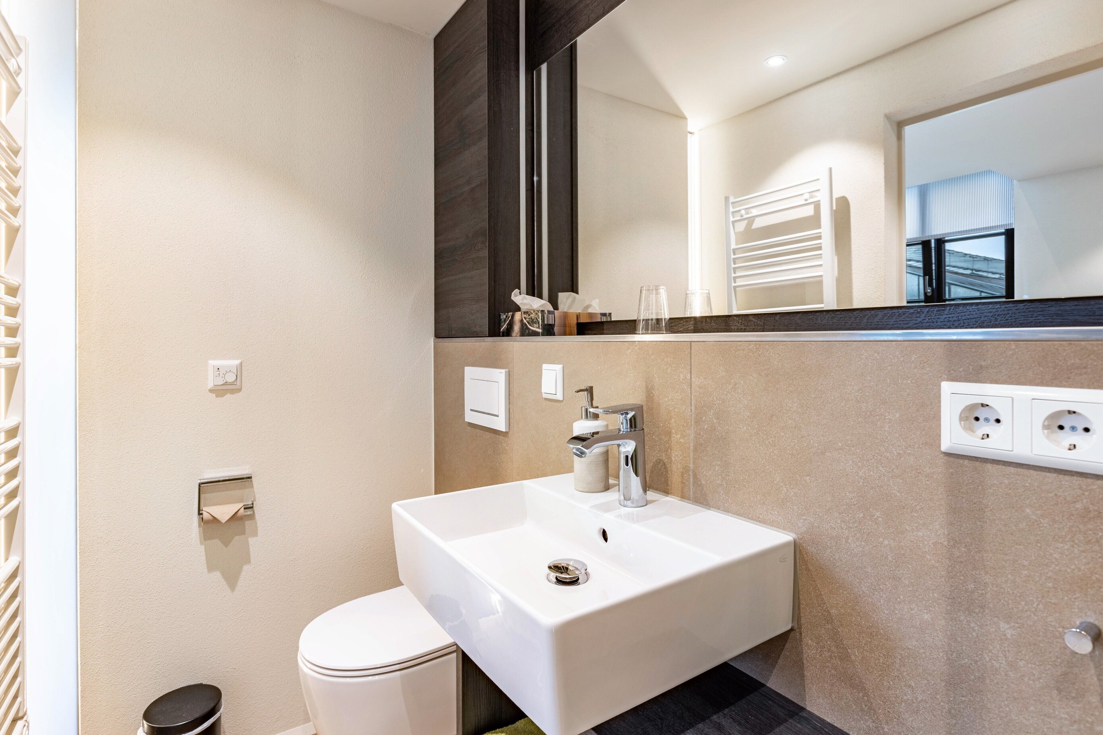 A modern bathroom with a white sink, mirror, and toilet.