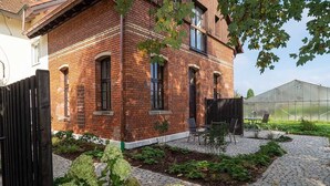 Una casa de ladrillo con un patio jardín, un invernadero y una puerta negra.