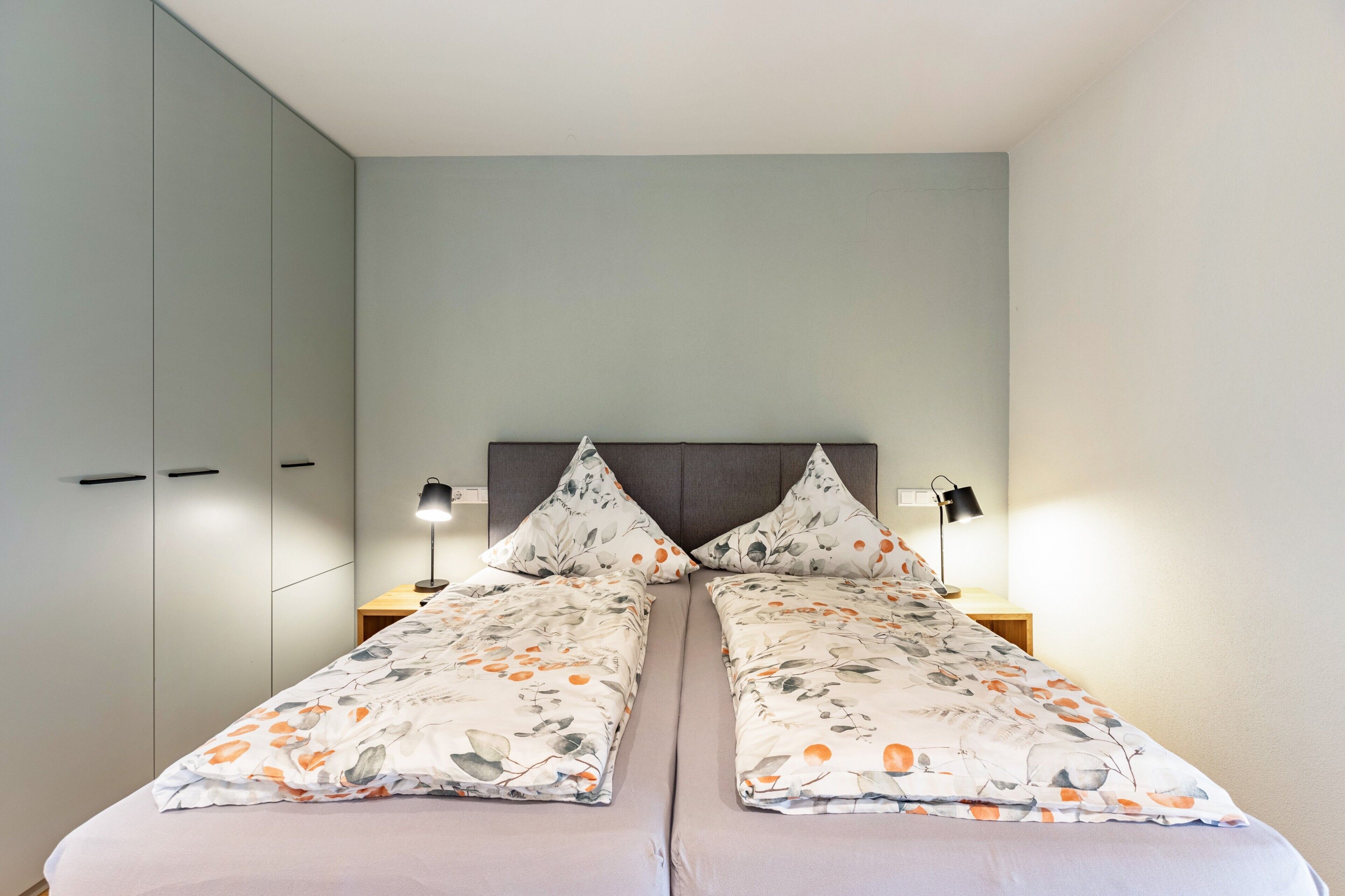 A double bed with floral bedding, two bedside lamps, and a grey headboard.