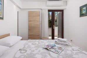 A hotel room with a bed, a wooden wardrobe, a small table, and a view of the outside through a glass door. - House Rose With Private Pool And Garden (Krk)