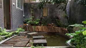 Un petit jardin avec un bassin, des marches en pierre et diverses plantes.