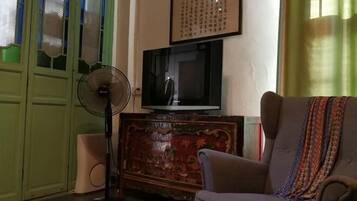 Una habitación con una televisión sobre un mueble de madera, un ventilador y un sofá.