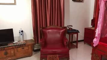 A living room with a red leather armchair, a wooden cabinet with a television, and a red curtain.