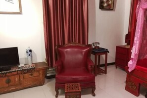A living room with a red leather armchair, a wooden cabinet with a television, and a red curtain. - Jinshidi Inn (Guangzhou)
