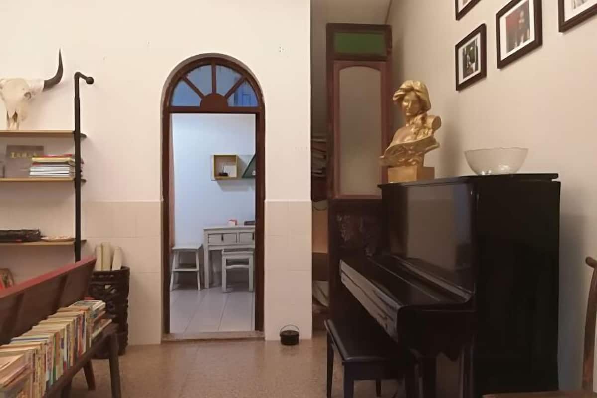 Huone, jossa on piano, kirjahylly ja rintakuva.