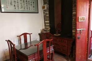 A traditional dining area with a wooden table and chairs, a stone wall, and a red door with a number plate. - Jinshidi Inn (Guangzhou)