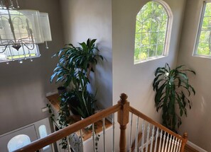 Un escalier avec une rampe en bois, un lustre et de grandes fenêtres donnant sur un paysage verdoyant.