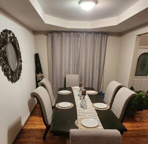 Une salle à manger avec une table en bois foncé, des chaises recouvertes d’un tissu beige et un miroir décoratif au mur.