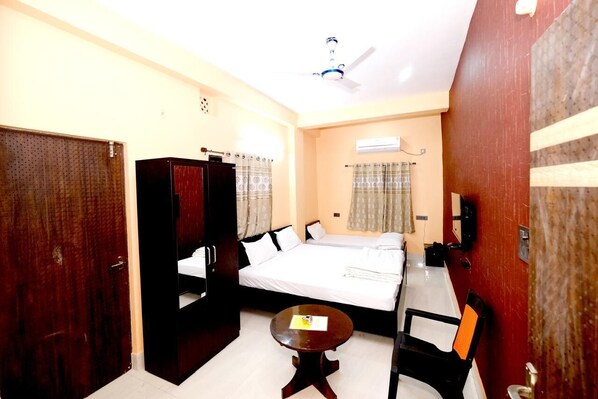 A hotel room with a bed, a desk, a chair, a wardrobe, and an air conditioning unit. - Hotel Krishna Paradise (Deoghar)