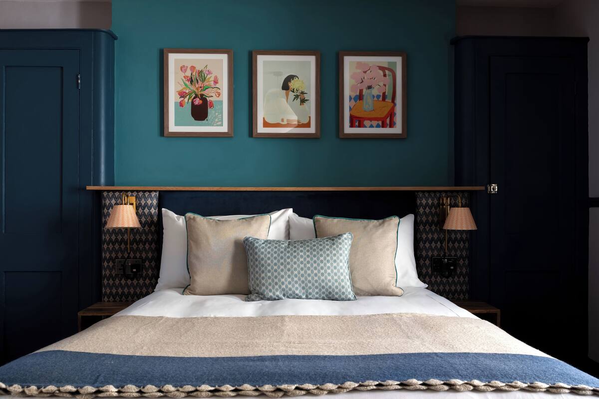 A bedroom with a teal wall, a bed with white bedding, and three framed artworks above the bed.