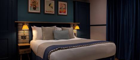 A neatly made bed with a headboard, two bedside tables with lamps, and three framed pictures on the wall.