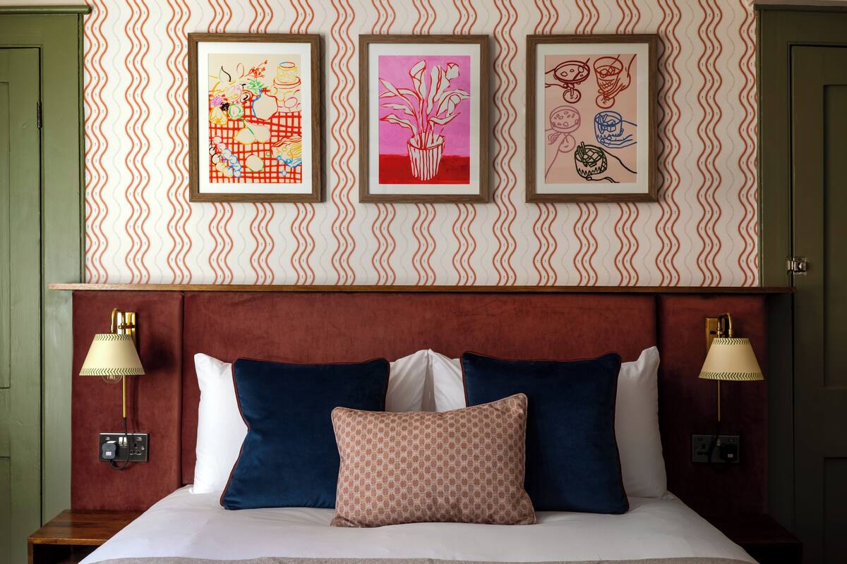 A hotel room with a bed, two wall-mounted lamps, and three framed artworks on the wall.