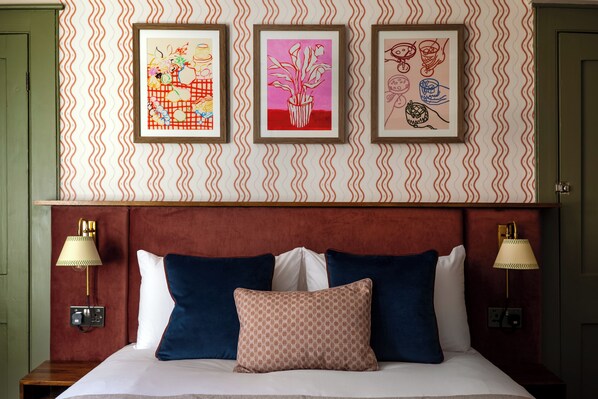 Habitación de hotel con una cama, dos lámparas fijadas a la pared y tres obras de arte enmarcadas.