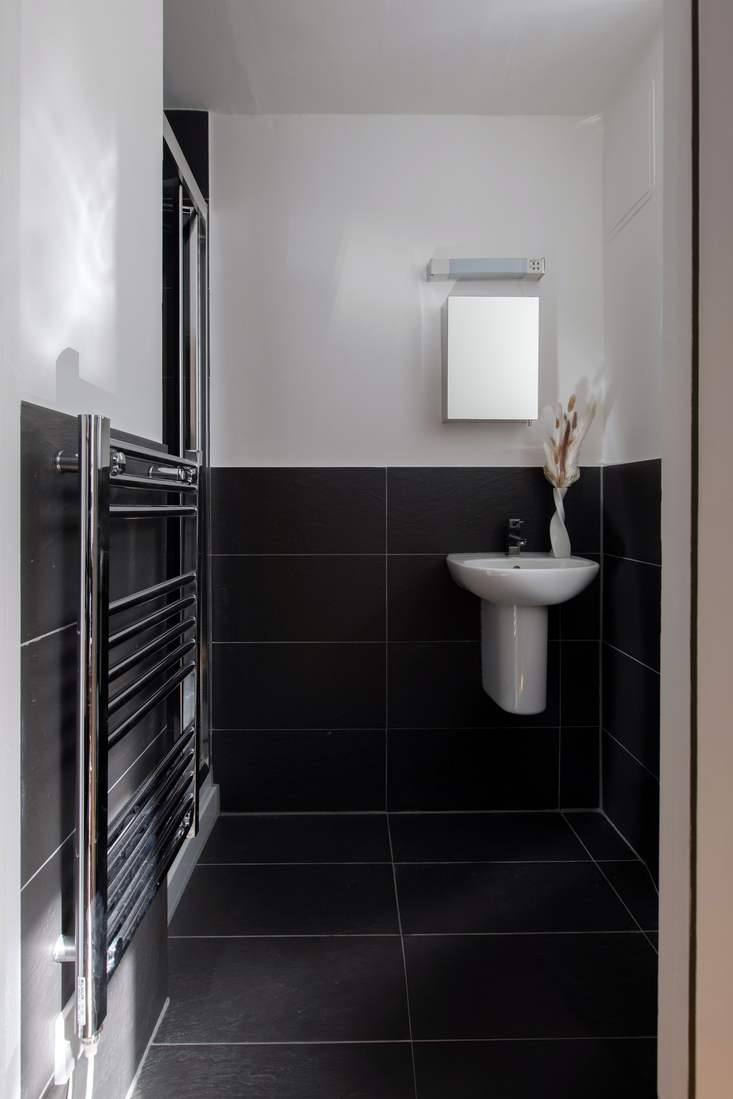 Un bagno moderno con pavimento piastrellato di nero, un lavandino bianco e un porta asciugamani.