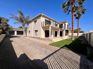 A two-story house with a balcony, a paved driveway, and palm trees. - Spacious 6-bedroom house, full equipped, in wonderful Swakopmund with WiFi (Swakopmund)