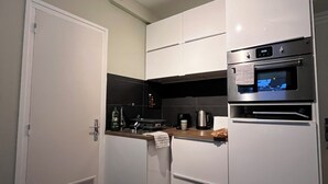 Cocina compacta con armarios blancos, horno empotrado y microondas.