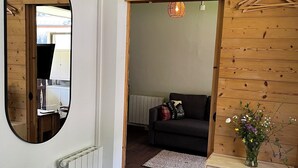 Una habitación con techo de madera, un espejo, un radiador, un sofá, un aparador y un florero con flores.