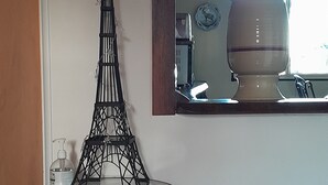 Une pièce dans laquelle on trouve une maquette de la Tour Eiffel servant d  ’élément décoratif, posée sur une table en verre, ainsi qu’une boîte de mouchoirs et un miroir qui reflète une partie de la cuisine.