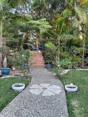 A garden pathway with steps leading to a seating area surrounded by various plants and trees. - Mapleton Peaceful Provence BnB (Mapleton)