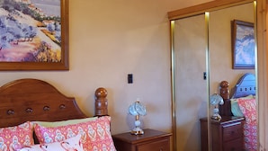 Une chambre à coucher avec un lit, une table de chevet, une lampe, un miroir et un tableau au mur.