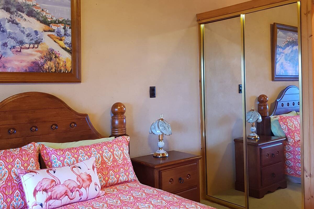 A bedroom with a bed, a nightstand, a lamp, a mirror, and a painting on the wall.